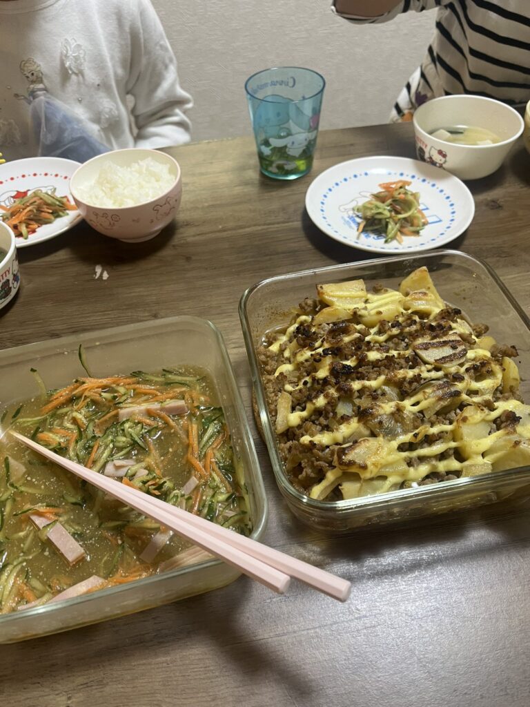 夕食を食べている写真です。ポテトとひき肉のマヨネーズ焼き、野菜の中華サラダです。保存容器からそのまま食べています。