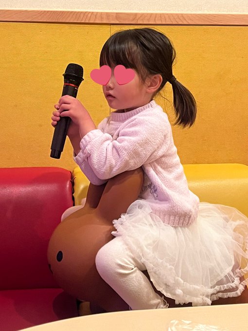 小さな女の子がミッフィーの乗り物に乗り、カラオケのマイクを持っている写真です。