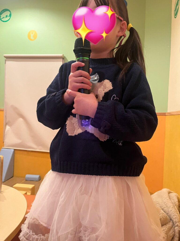 小さな女の子がカラオケで立ち上がって歌っている写真です。